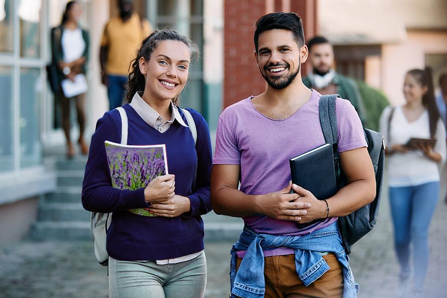 2 college students smiling. 一名学生穿着淡紫色的t恤，另一名学生拿着一本笔记本，背面画着一片薰衣草田.